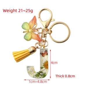 Detail of resin letter J keychain with dried flowers, orange butterfly and yellow tassel