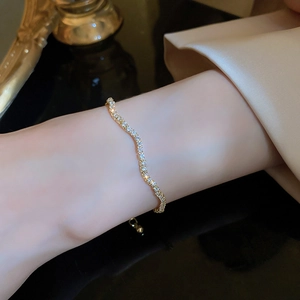Close-up of golden wavy adjustable bracelet with sparkling diamonds on female wrist