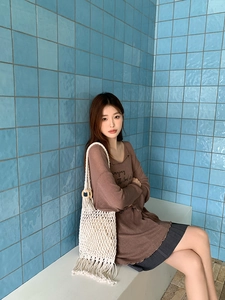 Detail of a cream woven straw bag with fringes styled with a brown long-sleeved shirt