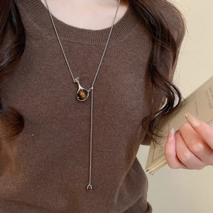 Macro shot of long Y-shaped necklace with tiger eye stone pendant on brown sweater
