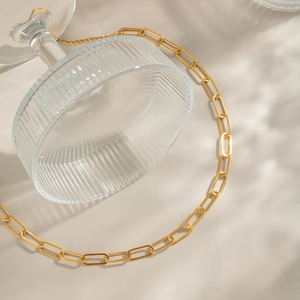 Détail d'un collier chaîne trombone doré étanche enroulé autour d'un verre texturé