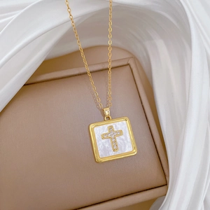 Detailed shot of a square shell pendant with a diamond-encrusted cross on a gold chain
