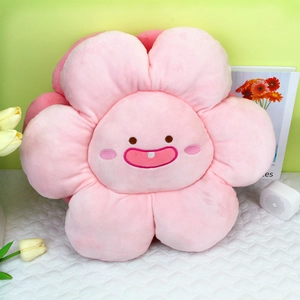 Coussin fleur en peluche rose avec visage souriant posé sur un support matelassé