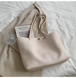 Detailed view of beige tote bag with litchi grain texture on trench coat backdrop