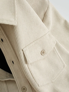 Detail of corduroy texture, button-down collar and chest pocket on cream casual shirt