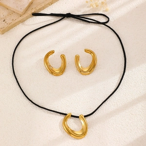 Detail of gold U-shaped pendant necklace and earrings set on a textured surface