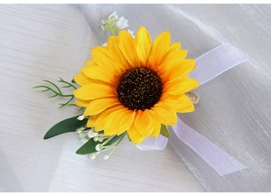 Detail of artificial sunflower corsage with silk petals, green leaves and ribbon