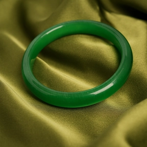 Close-up of green cat eye stone bracelet with smooth finish on olive silk fabric