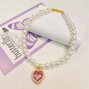 Detailed macro of pet pearl necklace with pink heart gemstone and gold lobster clasp