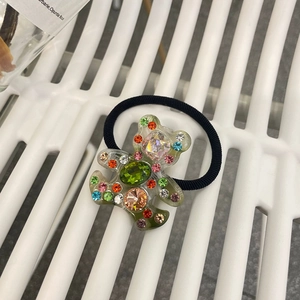 Détail d'un élastique ours en résine avec des strass colorés et un ruban élastique noir