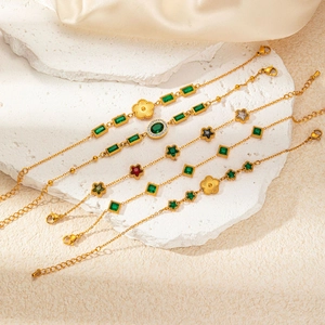 Close-up of gold titanium steel bracelets with emerald zircons on a white stone slab