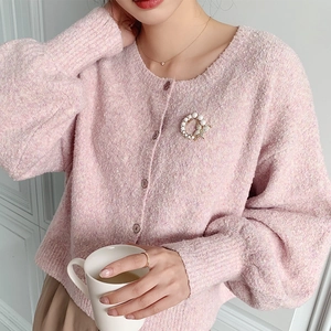Close-up of pearl butterfly brooch on soft pink textured knit cardigan with buttons