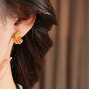 Détail d'une boucle d'oreille gourde plaquée or 18K avec cristaux orange sur modèle