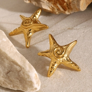 Detailed view of gold starfish earrings with spiral relief on a natural rock background