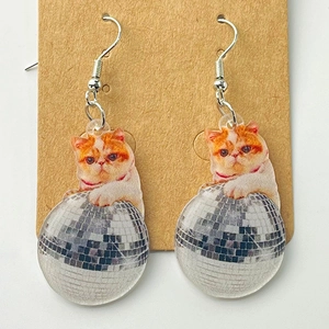 Detail of acrylic cat earrings featuring a pink disco ball design on kraft card