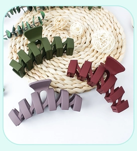Matte wavy hair claw clips in olive green, burgundy, and grey-purple on a woven mat