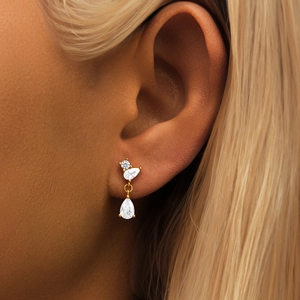 Close-up of gold drop earrings with three sparkling white zircons on a model's ear