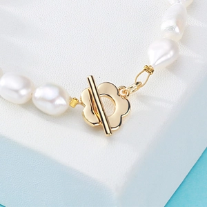 Baroque pearl necklace featuring a golden floral toggle clasp on white leather surface