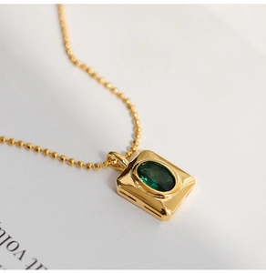 Macro shot of rectangular gold pendant with green crystal stone on a ball chain