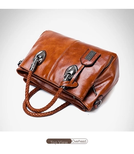 Detail of caramel brown Boston bag with woven handles and polished metal hardware