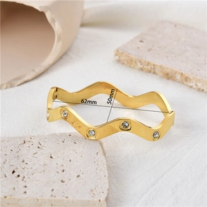 Detail view of gold wave bangle showing inner diameters of 62mm and 50mm with stones