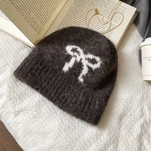 Detailed texture of charcoal grey plush knit beanie with white bow pattern on waffle fabric