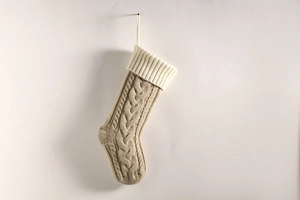 Detail of beige cable-knit Christmas stocking with cream ribbed cuff on plain wall
