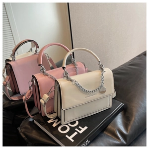 Pink and white chain shoulder bags on book showing leather texture and flap details