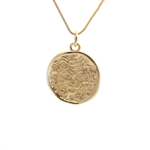 Macro detail of gold-plated Medusa head relief pendant with zircon accents on chain
