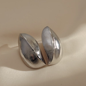Close-up of silver leaf-shaped earrings with fine brushed texture on silk fabric