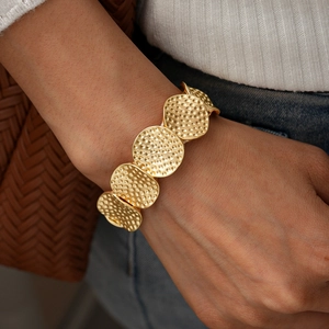 Detailaufnahme eines goldenen Metallarmbands mit Hammerschlag-Textur am Handgelenk