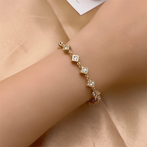 Detailed view of a gold cubic zircon bracelet on a wrist with silk fabric background