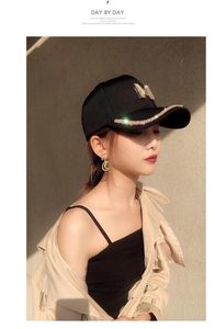 Detail view of black baseball cap featuring rhinestone brim and metal M logo on the front
