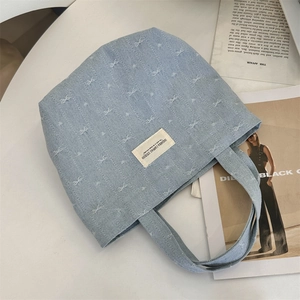 Close-up of denim tote bag with white bow embroidery and branded woven label