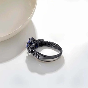 Close-up of gothic black plated ring featuring an oval blue gemstone and hollow patterns