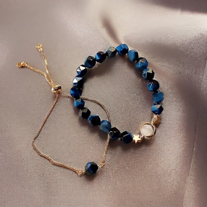 Elegant emerald blue beaded bracelet set with gold star charms on grey silk background