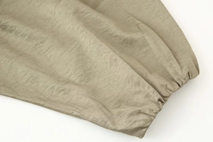 Close-up of olive green bomber jacket showing elastic ribbed cuff and nylon fabric texture