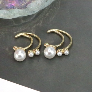 Close-up of gold double-arch earrings featuring three white pearls on a dark background