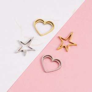 Polished hollow heart and star metal pendants in gold and silver finishes on a pink background