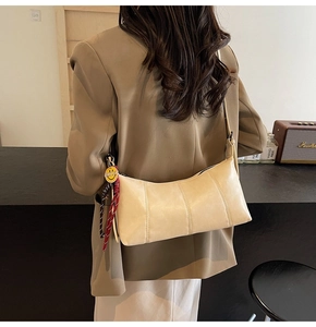 Detail of cream beige underarm bag with smiley charm on a shoulder strap in cozy setting