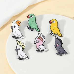 Lot de six broches perroquet en émail coloré présentées sur une assiette blanche