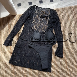 Flat lay of black three-piece bikini set with sheer lace long sleeve cover-up and high waist bottoms