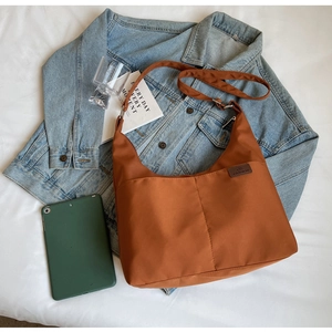 Detail of a brown canvas Hobo bag with adjustable strap and front pocket on a bed