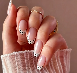 Detail of French almond press-on nails with nude base, white tips and black polka dots