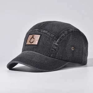 Close-up of black washed denim camp hat with brown patch and bronze metal ring detail