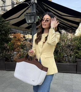 Close-up of a pale yellow round neck single-breasted blazer styled with a canvas handbag