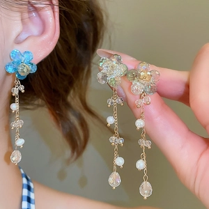 Detail view showing elegant floral tassel earrings with blue beads and pearls on model