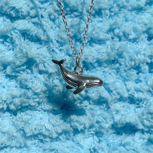 Close-up of minimalist 925 silver whale tail pendant on a blue plush background