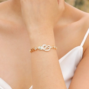 Detailed close-up of golden snake bracelet with green gem eyes and heart links