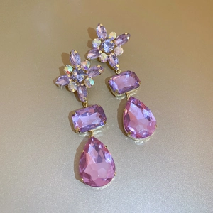 Macro shot of purple crystal floral drop earrings with a golden finish on a gold surface